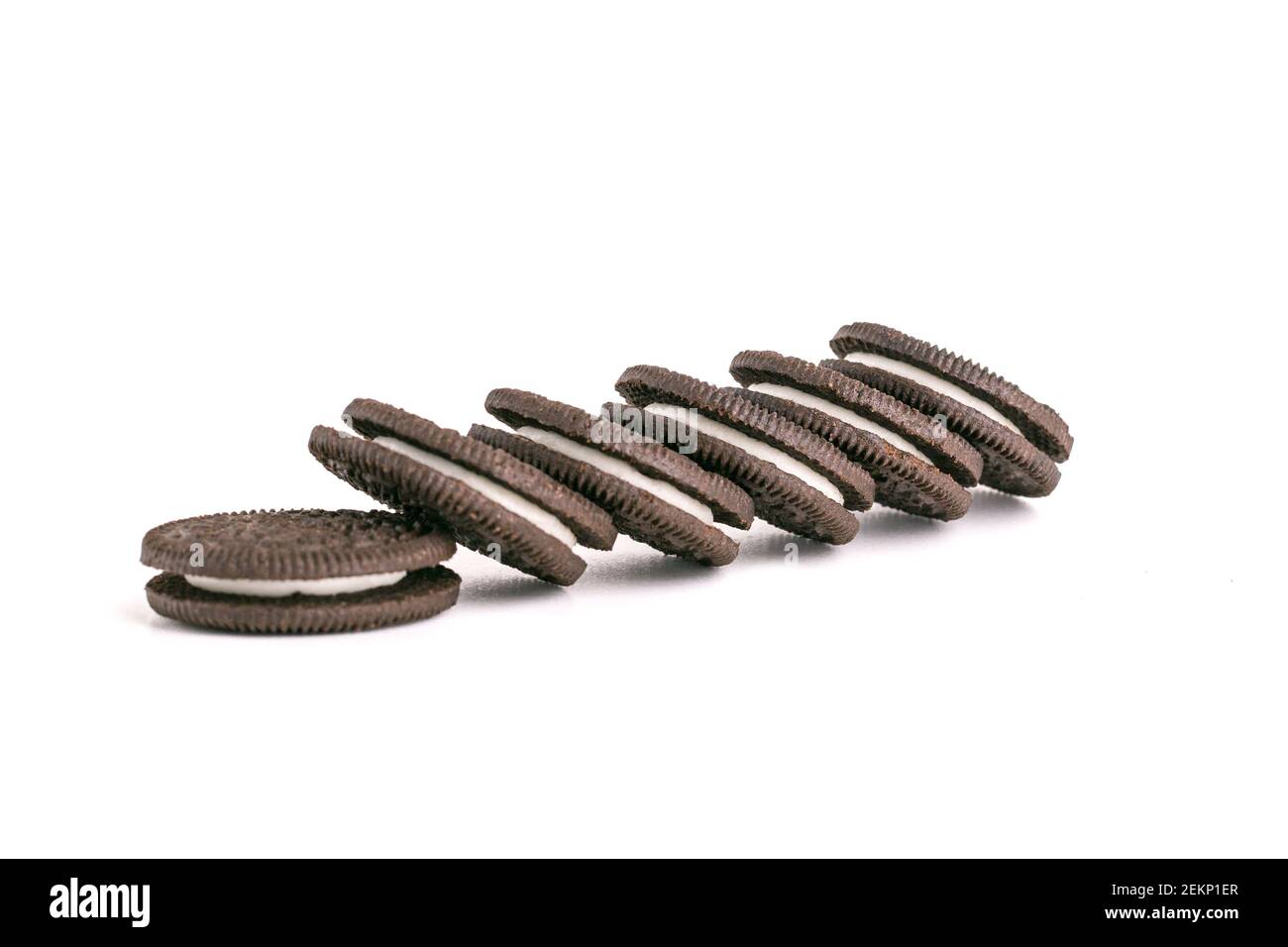 Chocolate black thin cookie with white filling, delicious milk sweet cookie scattered on a white background Stock Photo