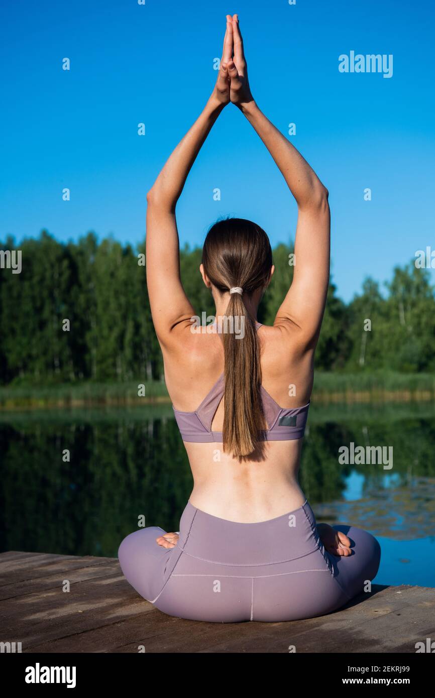 Young female practicing yoga against the sky on a sunrise. Pretty slim woman performs an exercise. Healthcare, meditaion, welness, mindfulness concept Stock Photo