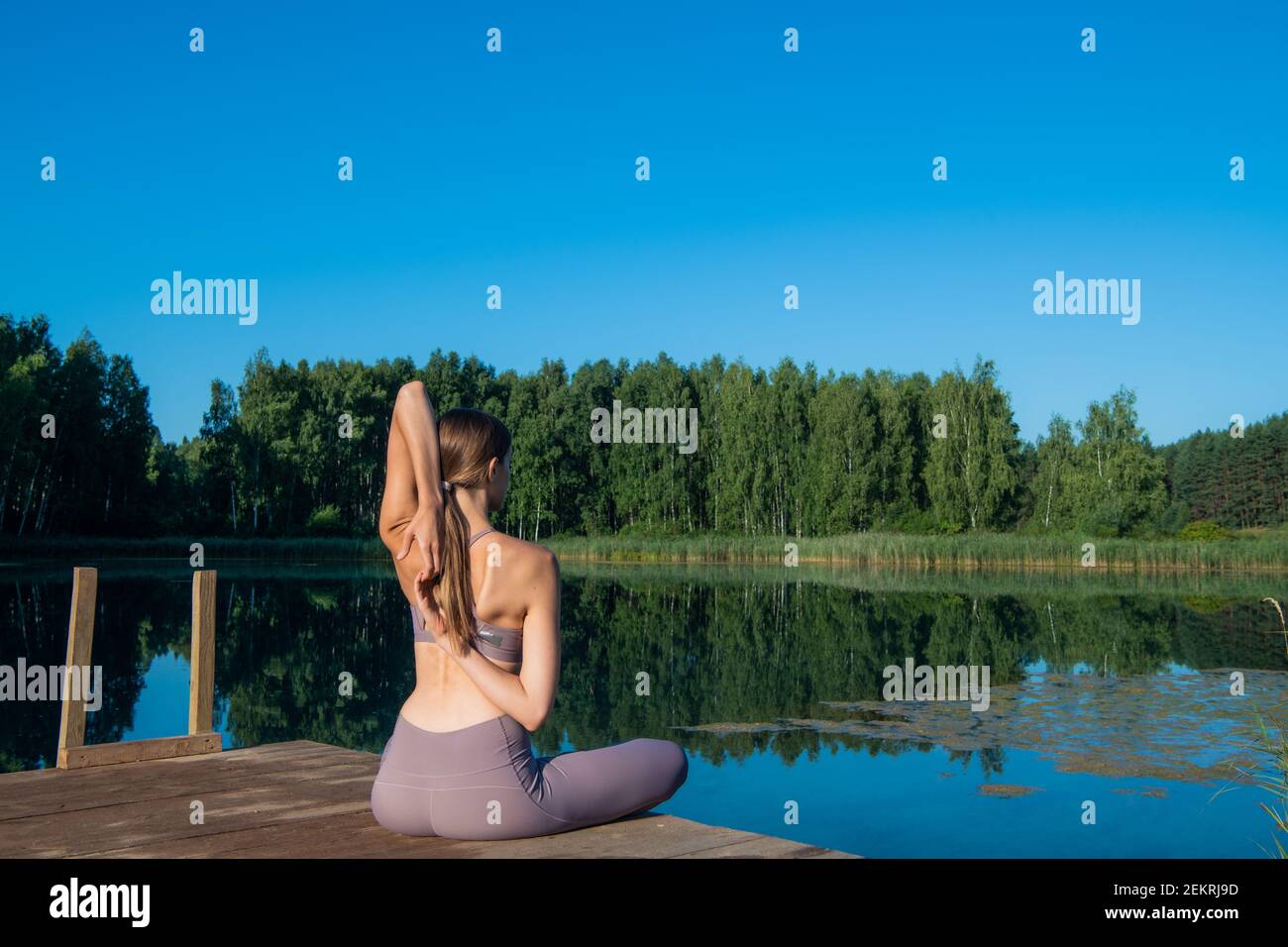 Young female practicing yoga against the sky on a sunrise. Pretty slim woman performs an exercise. Healthcare, meditaion, welness, mindfulness concept Stock Photo