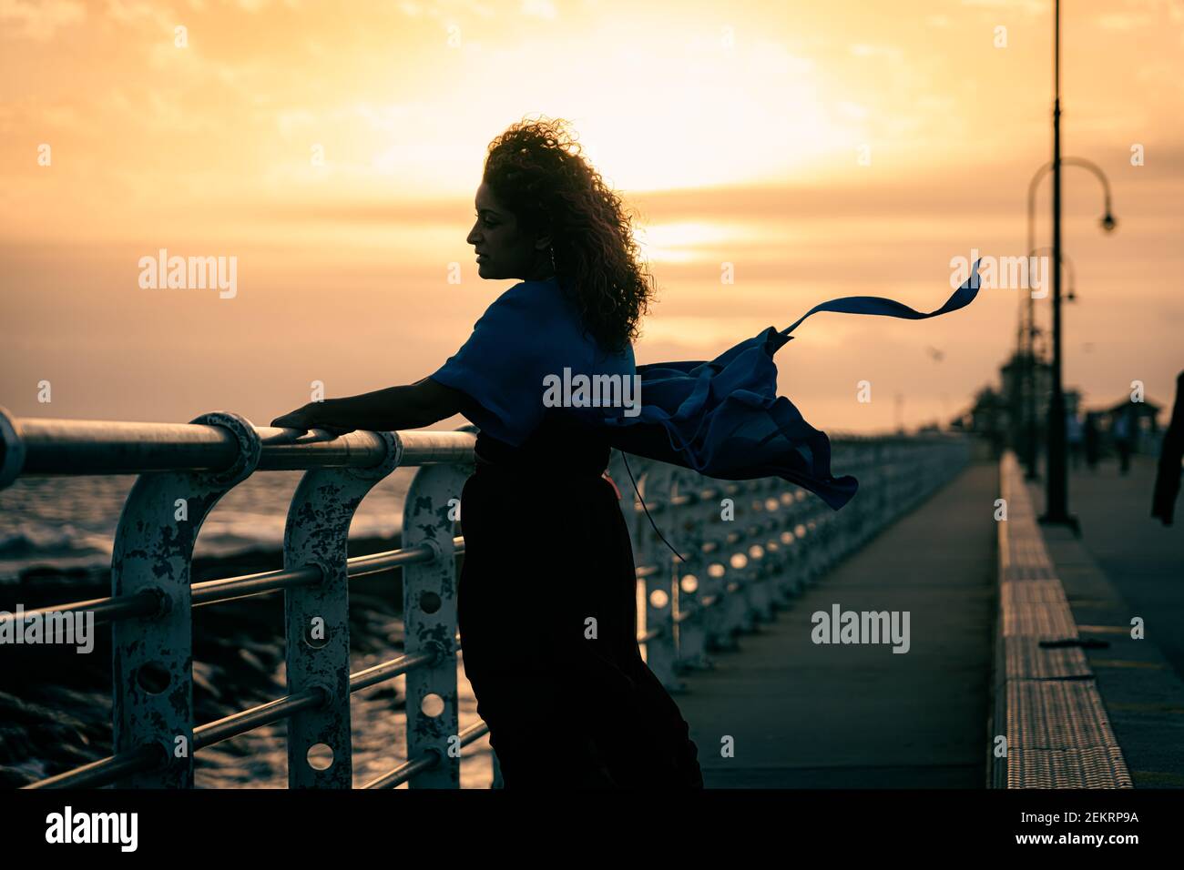 Woman in blue dress and with pink hair at sunset on St Kilda beach pier