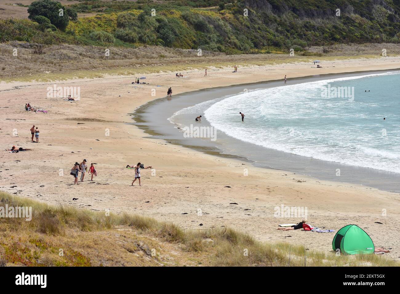 Sandy beach in small bay at low tide with holidaymakers sunbathing and playing in surf. Stock Photo
