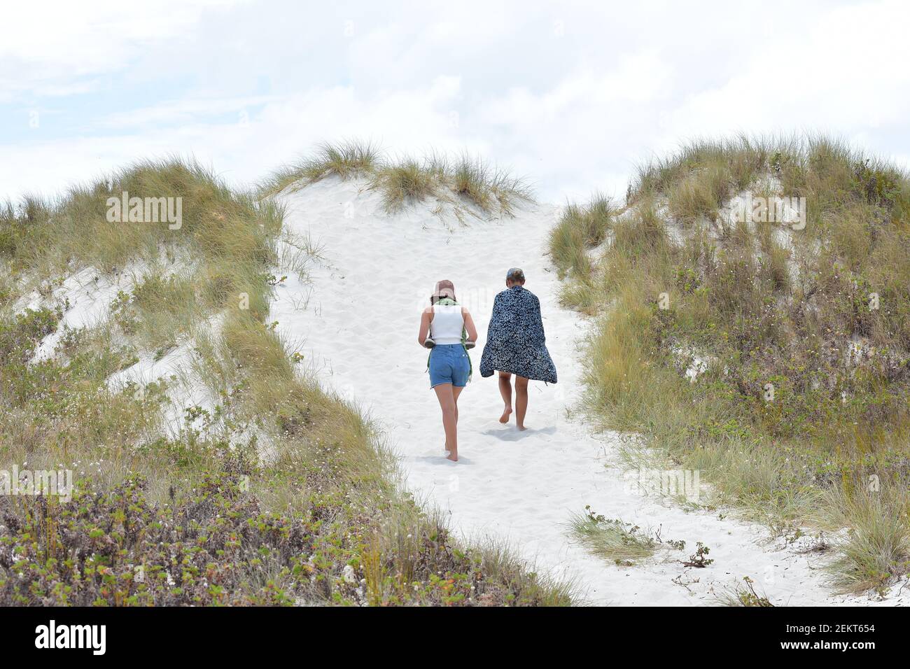 Two females in summer clothing walking up white sand dune footpath. Stock Photo