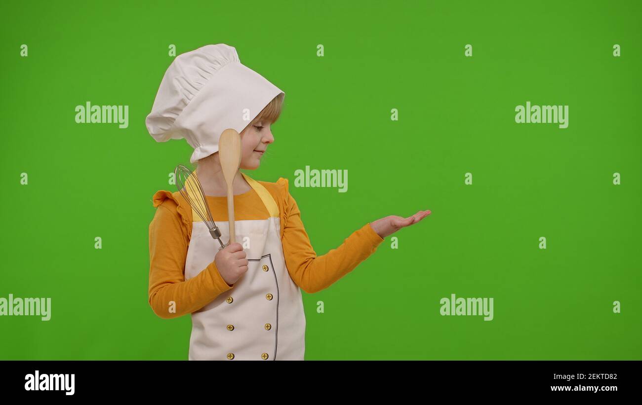Child girl dressed in apron and hat like chef cook pointing at right on ...