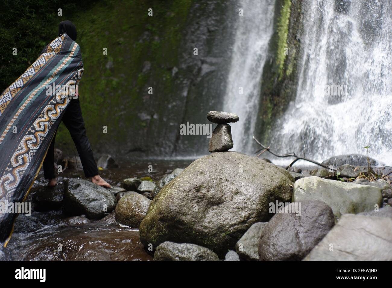 play rock balance in the river water flow. relaxation in the cool tropical wilderness. balance rock with waterfall background and woman traveler Stock Photo