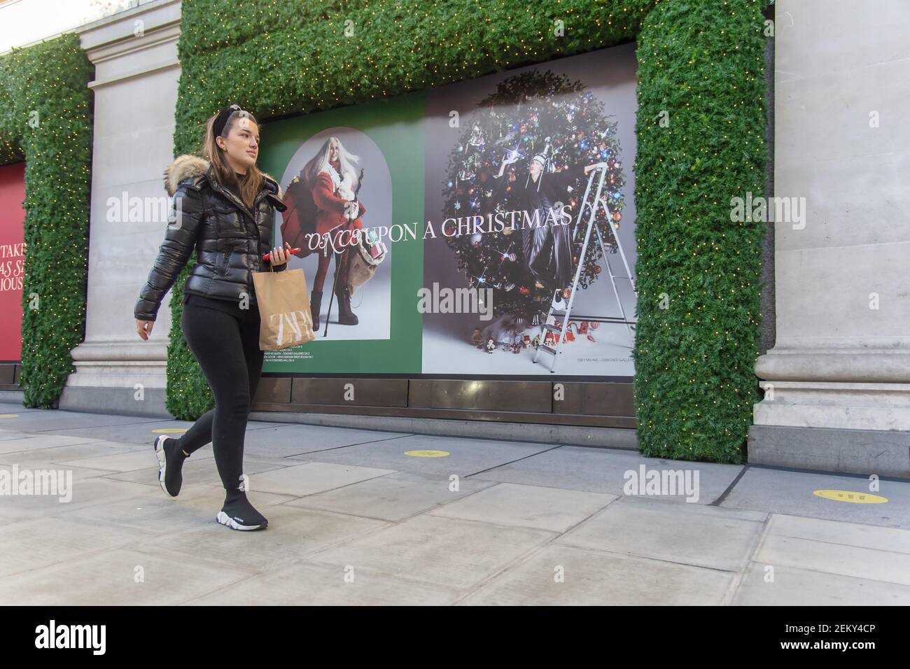 A woman carrying a Zara bag walks past a Christmas poster outside the