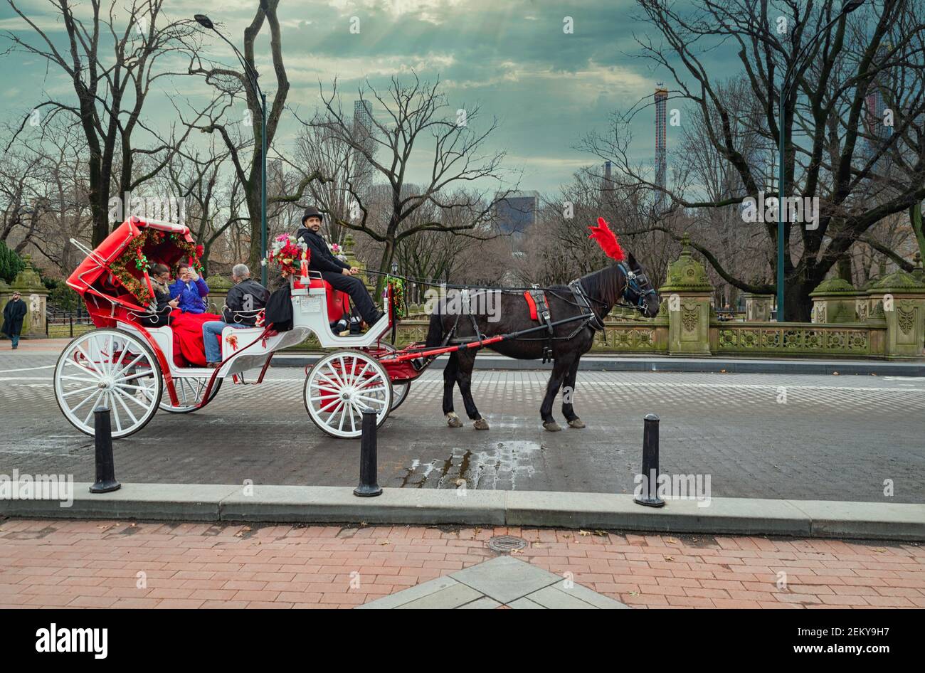 A horse and buggy carriage with coachman in Central Park New York city with visitors, Sunset view with skyline and clouds in the sky in background Stock Photo