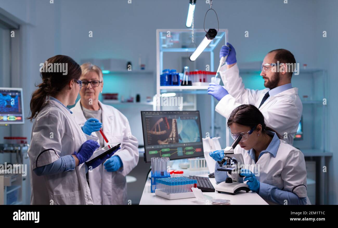 Team of scientific investigators conducting experiments in lab using microscope and micropipette