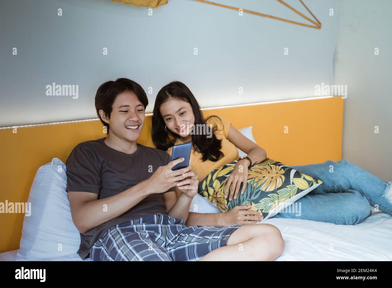 Beautiful young couple using smart phone and smiling while spending time in bed at home Stock Photo