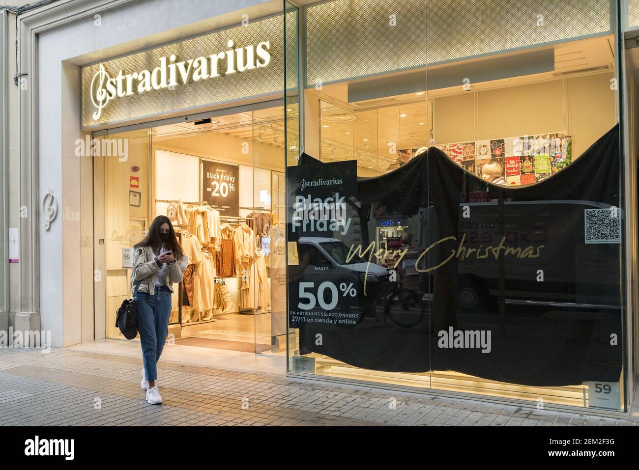 A woman wearing a face mask as a precaution against the spread of covid-19  walking past an advertising banner of Black Friday in front of the  Stradivarius shop during the heavy rain. (
