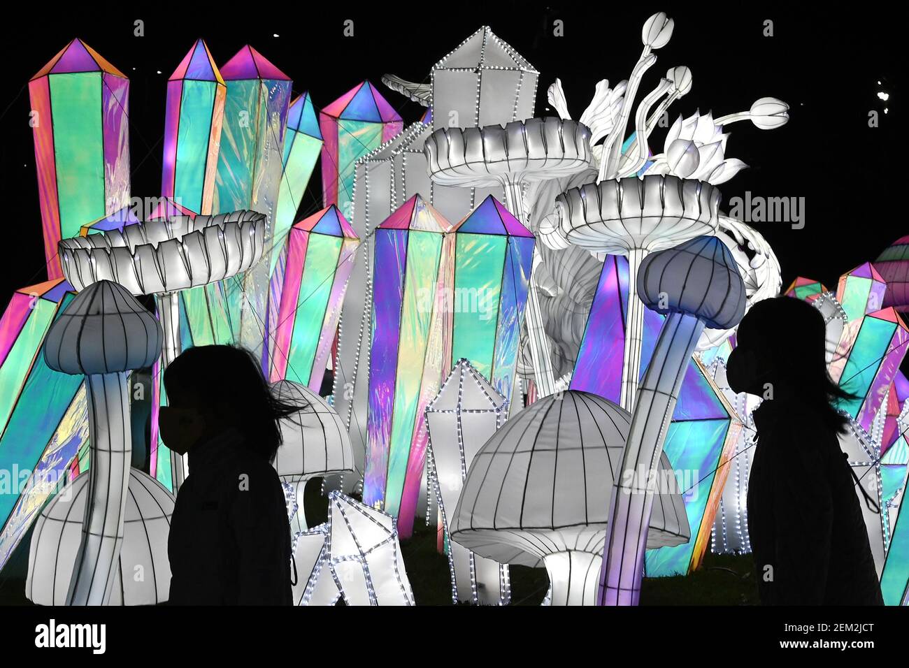 Visitors wearing masks walk past displays of crafted lights in the