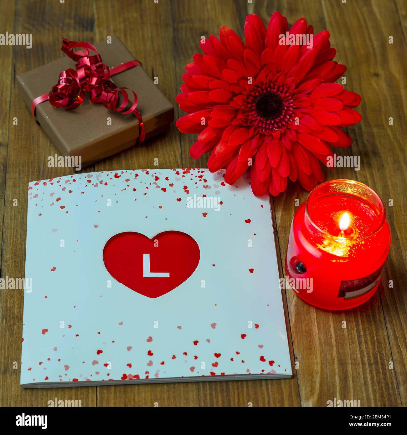 Composition with gift box and book with heart-shaped cover and letter L highlighted on red background and red flower Stock Photo