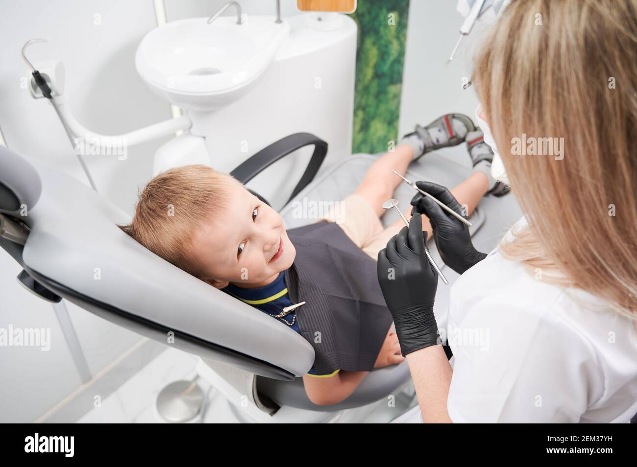 Adorable male child looking at camera and smiling while female dentist