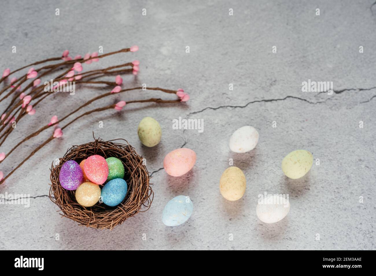 Colourful Easter eggs in bird's nest with decorative willow branches on gray cement background Stock Photo
