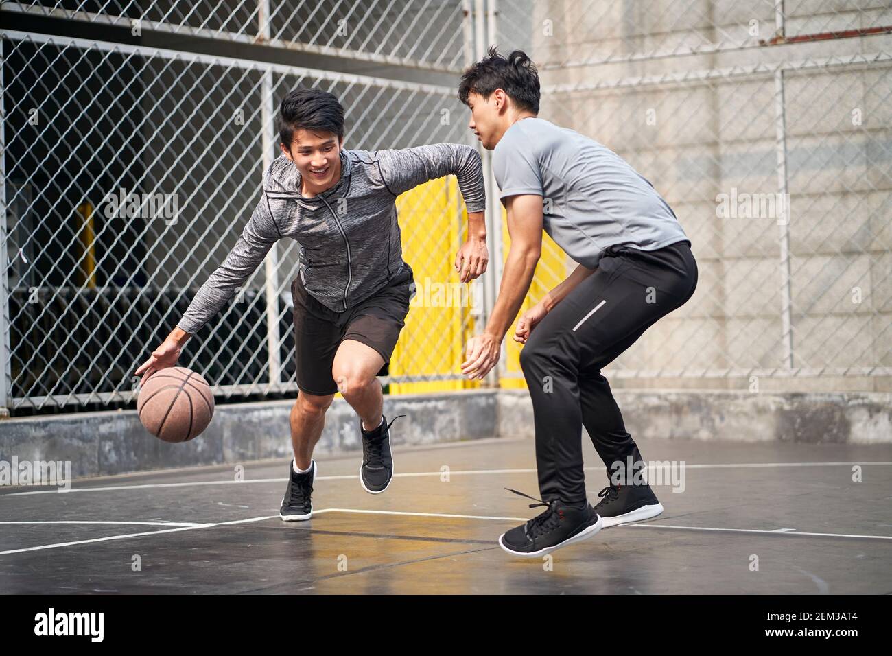 two young asian adult men playing one-on-one basketball on outdoor court Stock Photo
