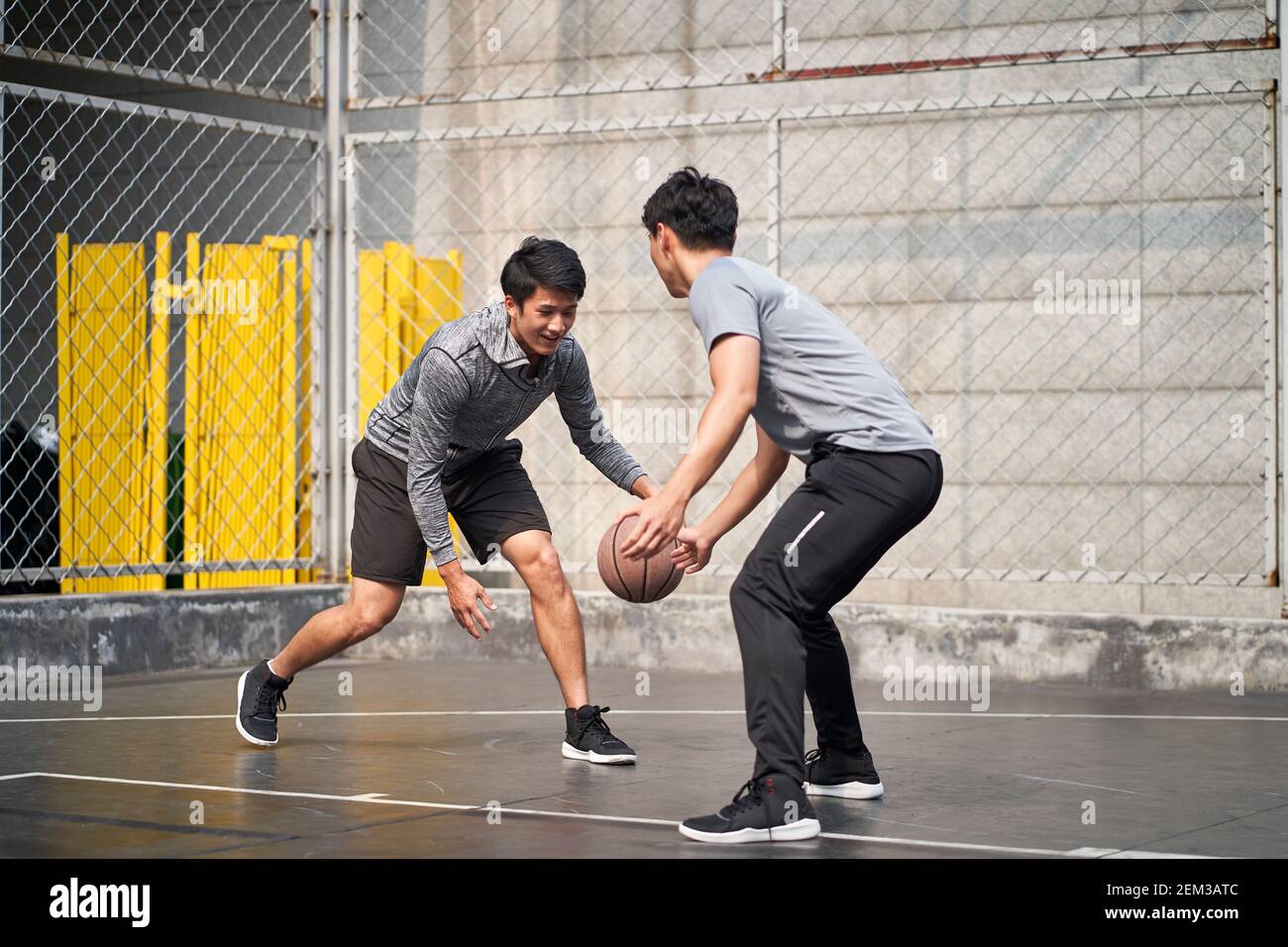 two young asian adult men playing one-on-one basketball on outdoor court Stock Photo