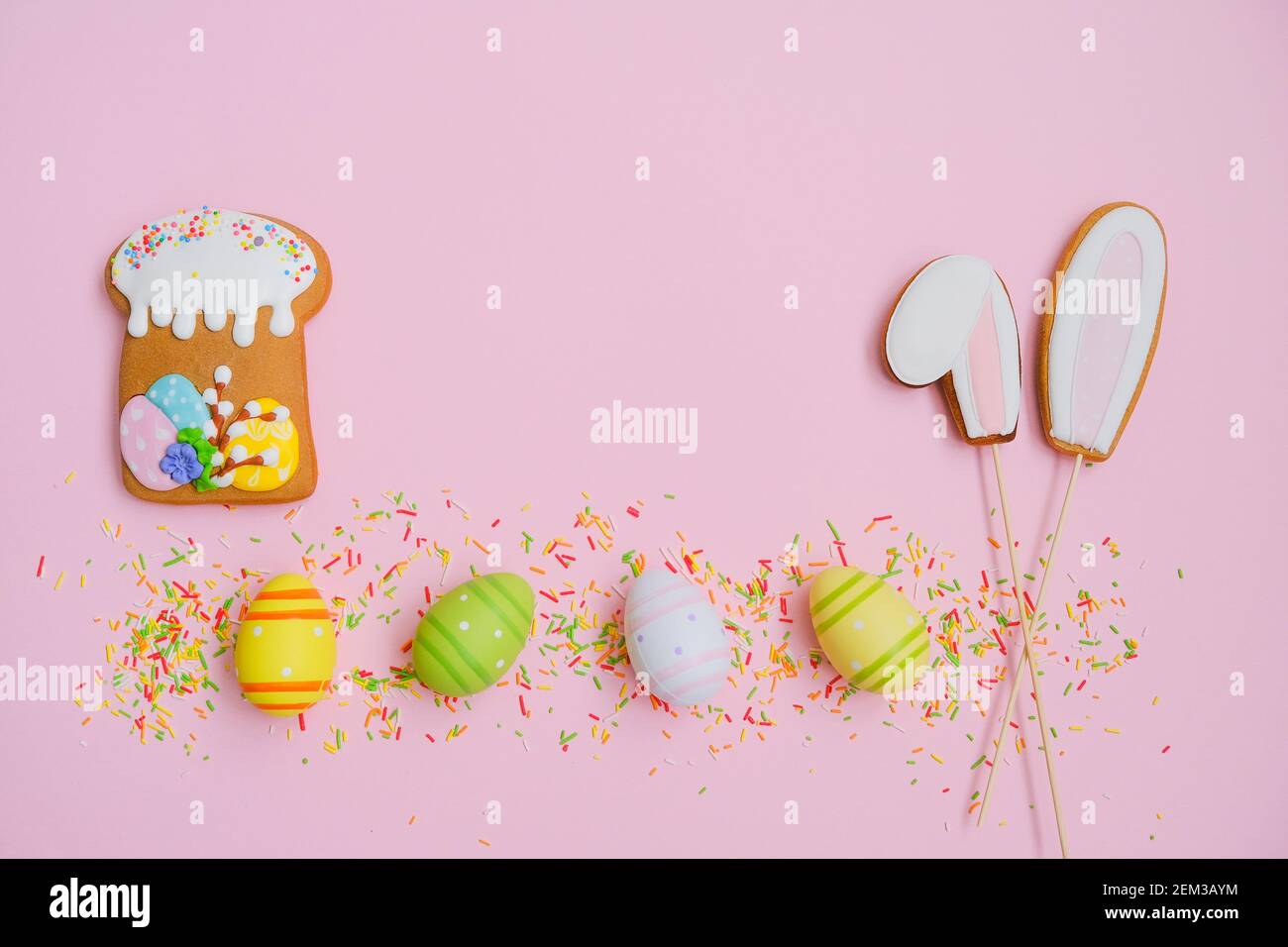 Easter cake, eggs, sugar sprinkles and cookies bunny ears on a pink background. Sweets for celebrating Easter. Stock Photo