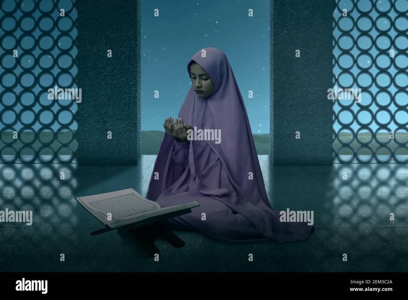 Asian Muslim woman in a veil sitting while raised hands and praying in ...