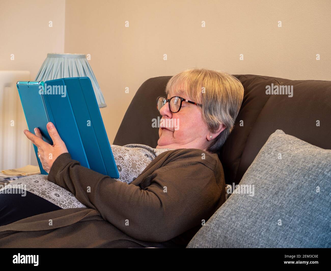 Senior woman resting on a settee engrossed in her tablet computer, UK Stock Photo