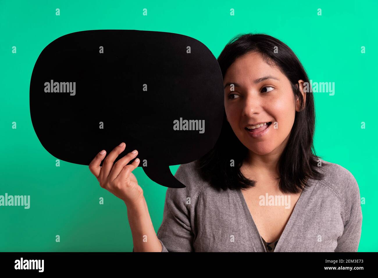young hispanic woman smiling and looking at black empty bubble with surprise, concept of ideas and imagination. empty cloud with copy space. green stu Stock Photo