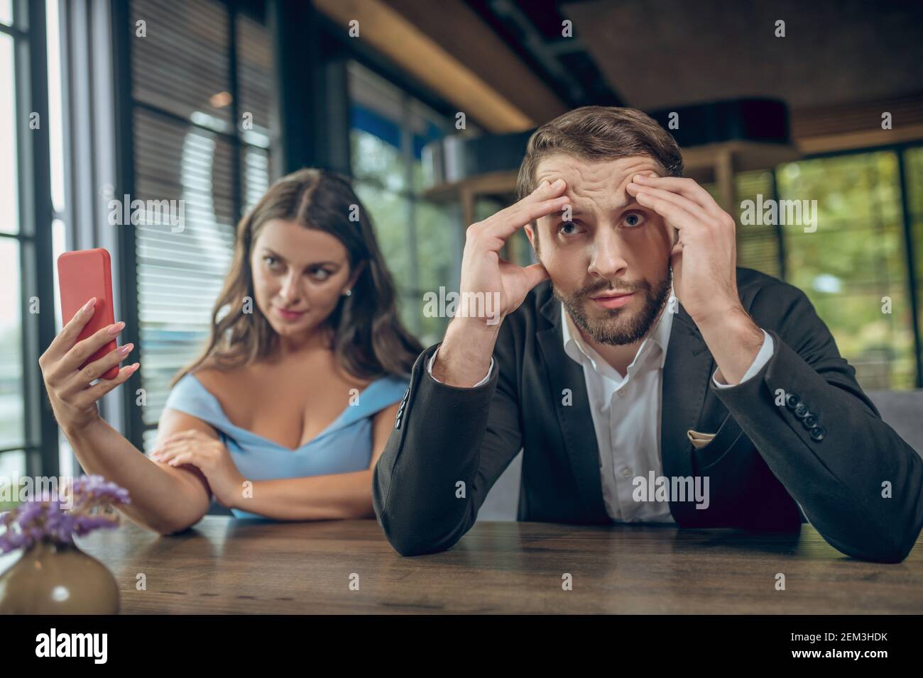 Woman taking selfie and disgruntled bored man Stock Photo