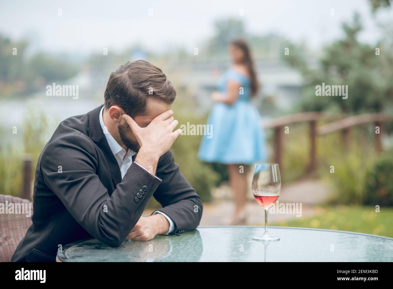 Unhappy man at table and woman in distance Stock Photo