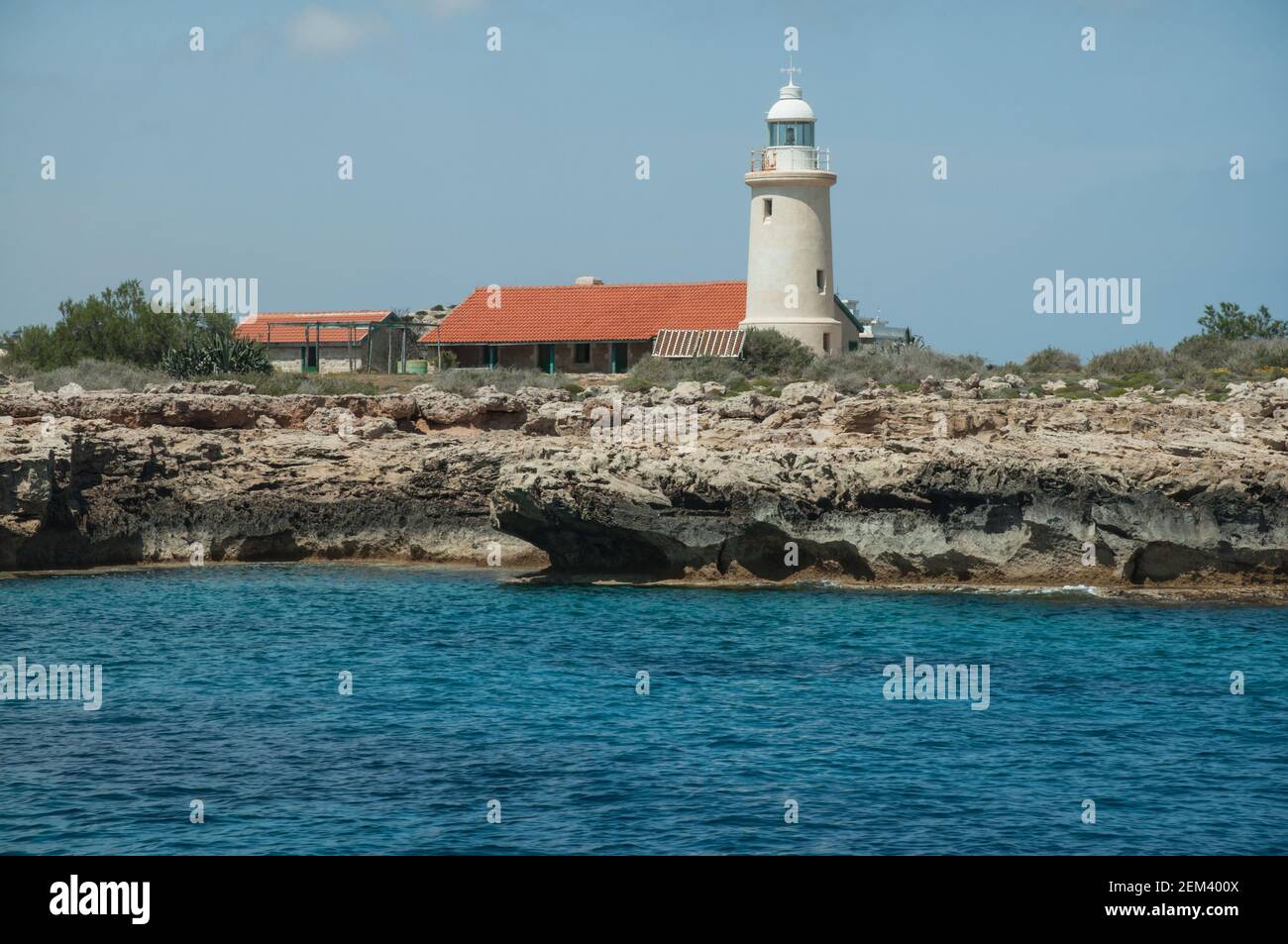 View of the small white lighthouse on the rock from sea . Landscape with turquoise sea and grottoes on coast of Cyprus Stock Photo
