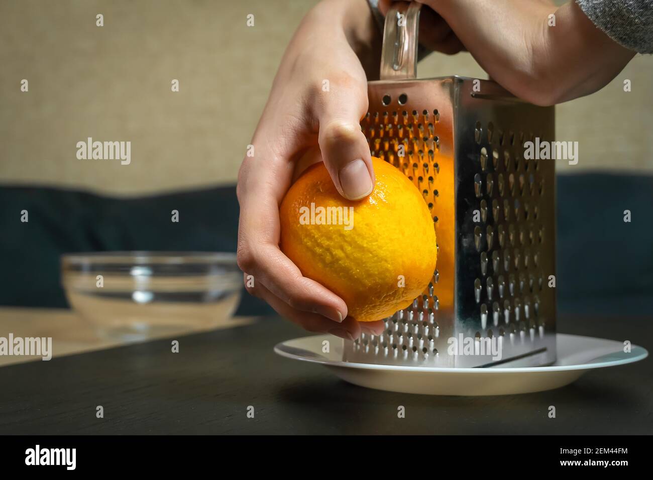 Female chef grates orange zest with a grater closeup in the kitchen
