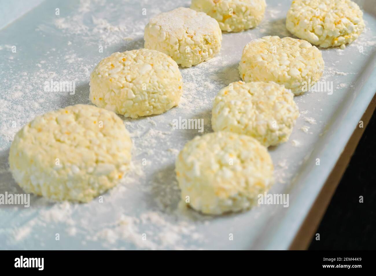 Lots of cottage cheese pancakes on a white tray with flour close up before frying in a frying pan. Selective Focus Stock Photo