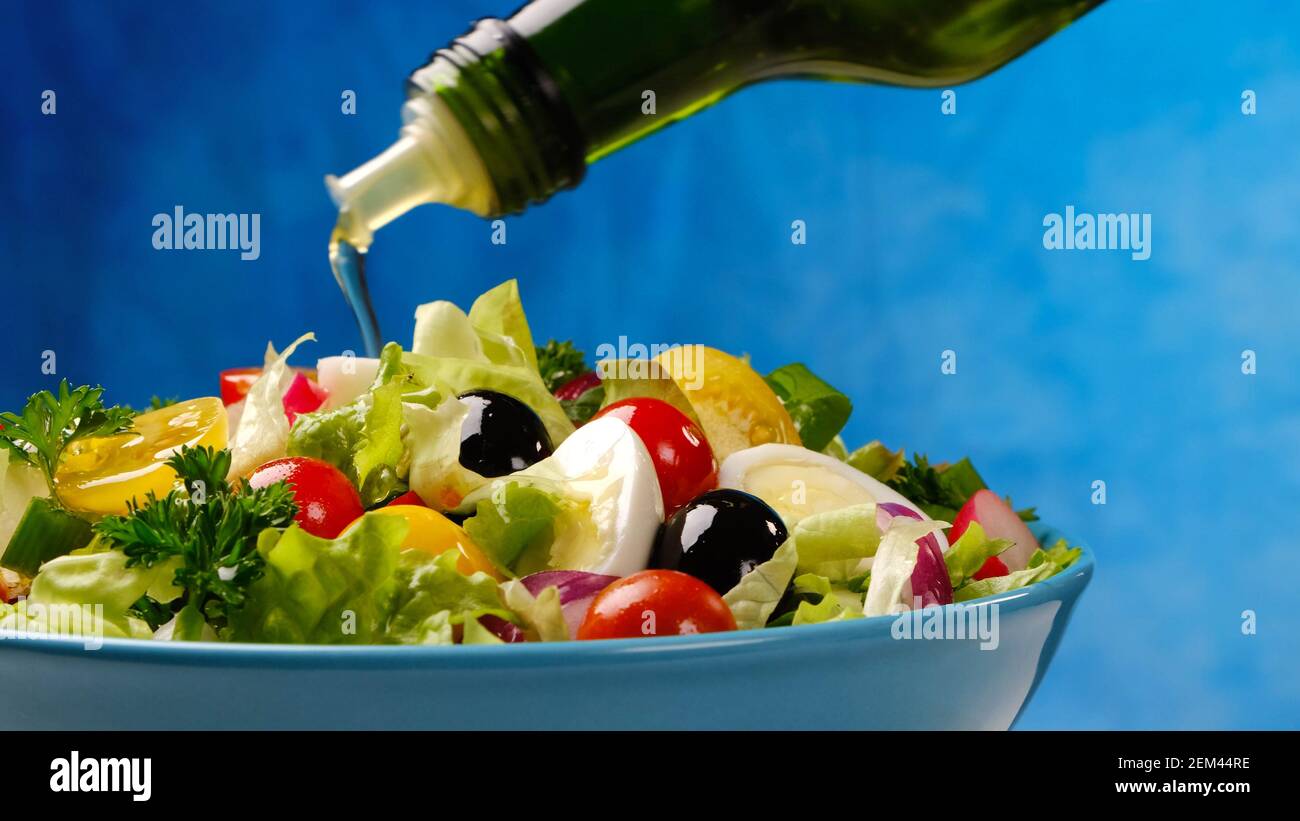 Olive oil pouring from bottle onto fresh vegetable salad Stock Photo