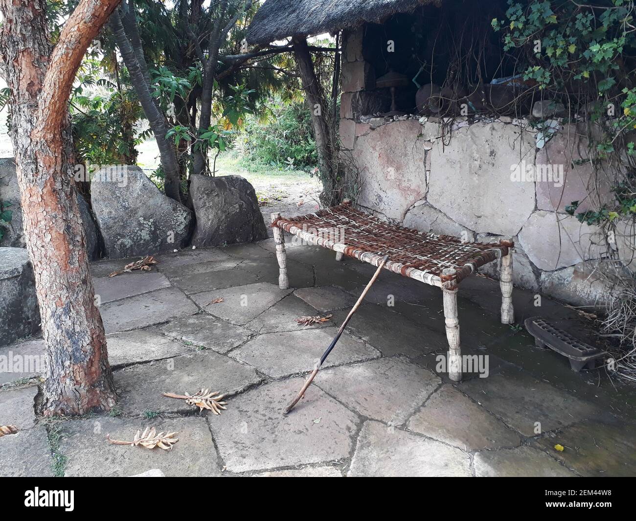 Traditional African wood frame and leather strap bench outside a thatched hut Stock Photo