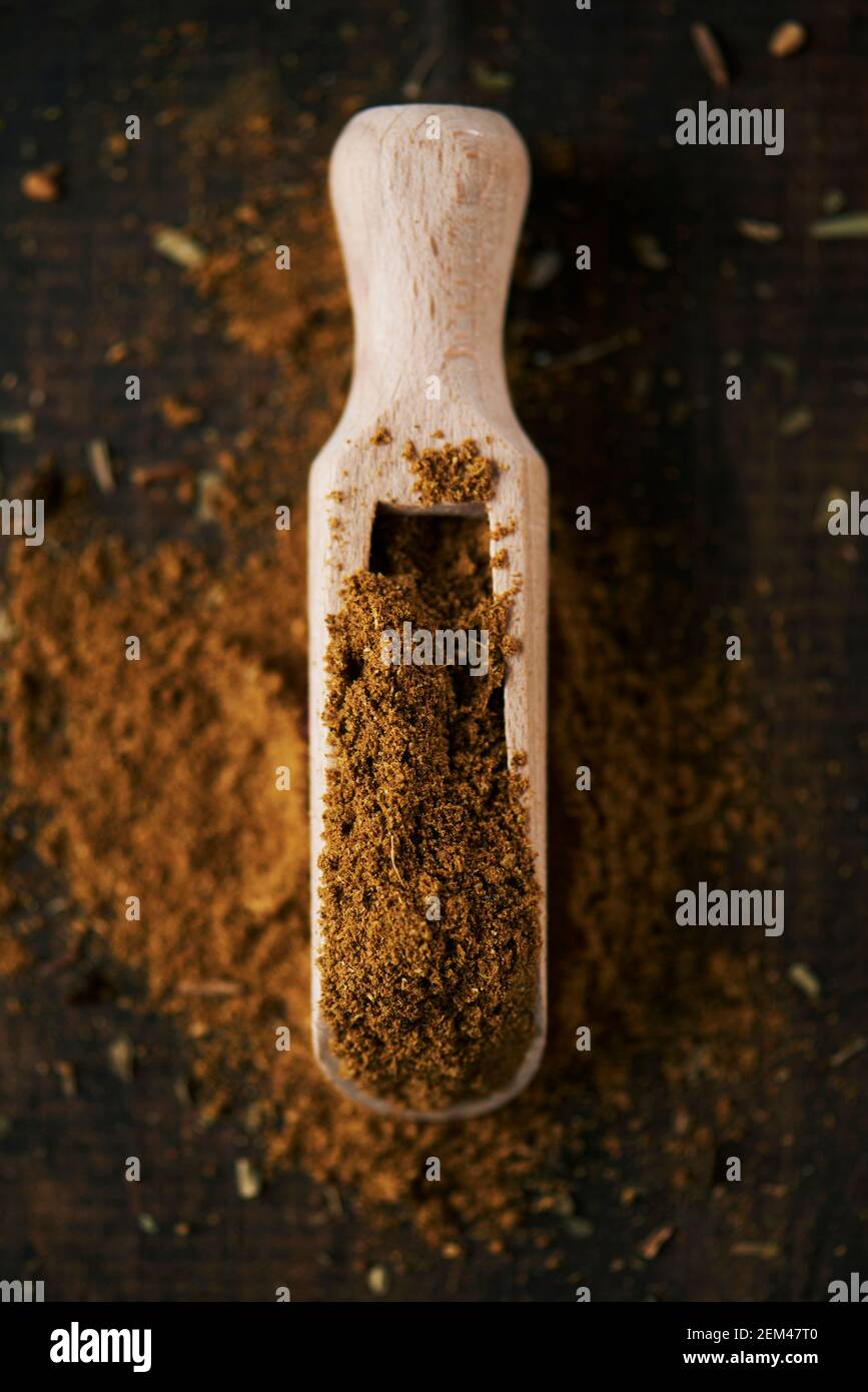 high angle view of a wooden measuring scoop full of garam masala, a popular seasoning in the south-asian cuisine, on a dark wooden surface Stock Photo