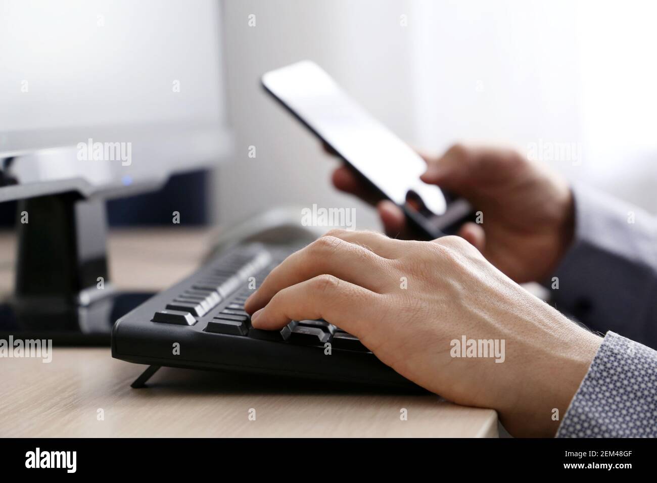 Man using smartphone on PC keyboard background. Concept of online communication, office or home work and payment Stock Photo