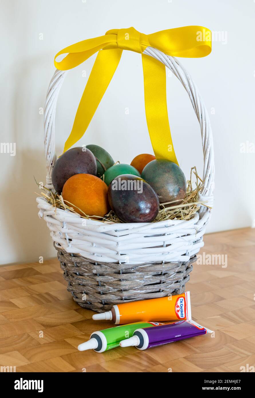 Still life of marbled coloured Easter eggs in willow basket with yellow ribbon and Dr Oetker food colouring Stock Photo