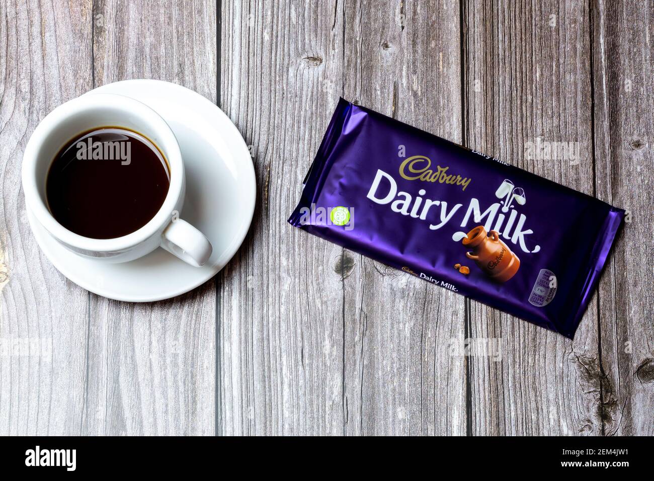 A Bar of Cadbury Dairy Milk chocolate lad on a wooden table next to a cup of coffee Stock Photo