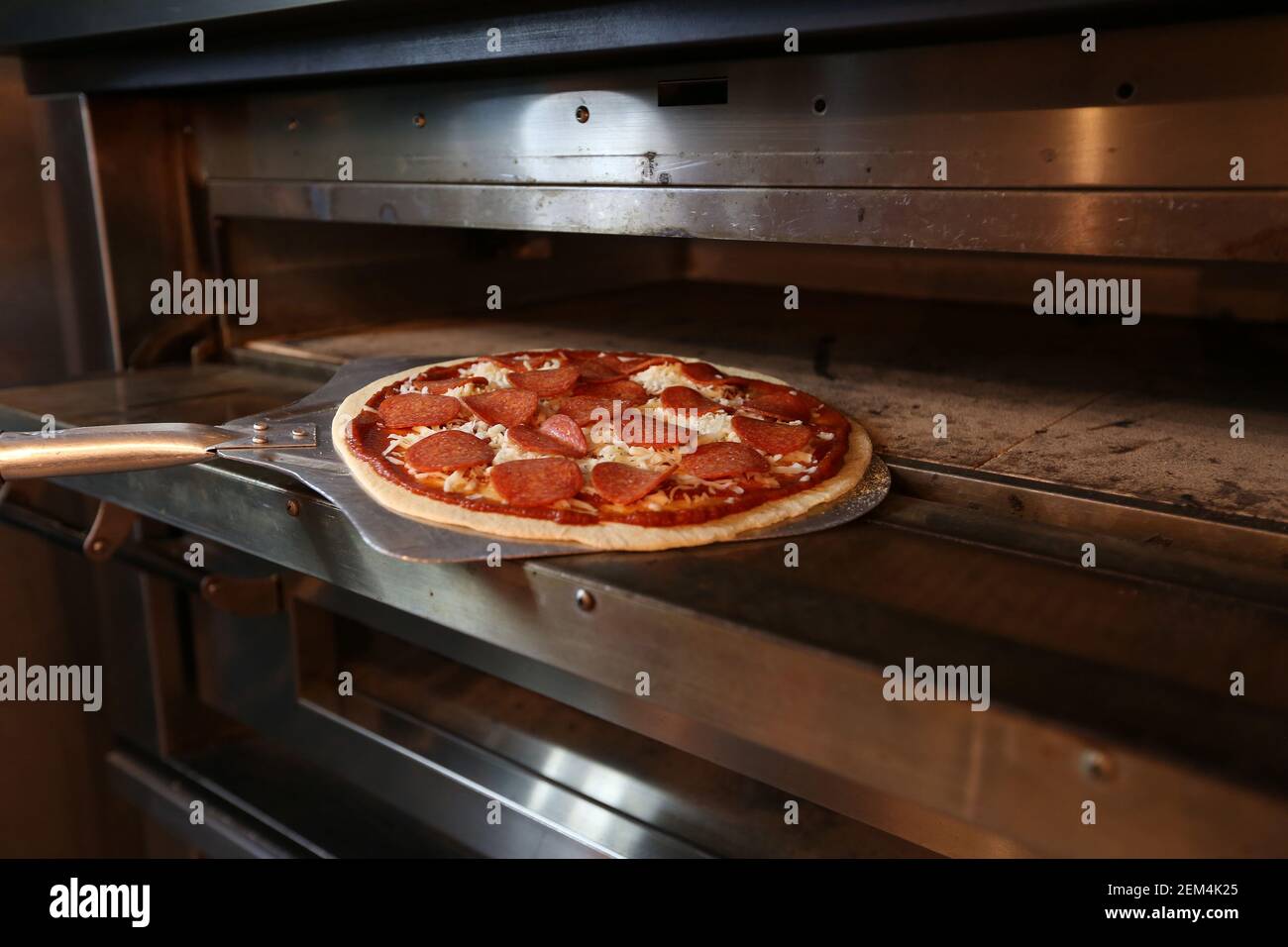 A pepperoni pizza being put into the oven to cook in a restaurant Stock Photo