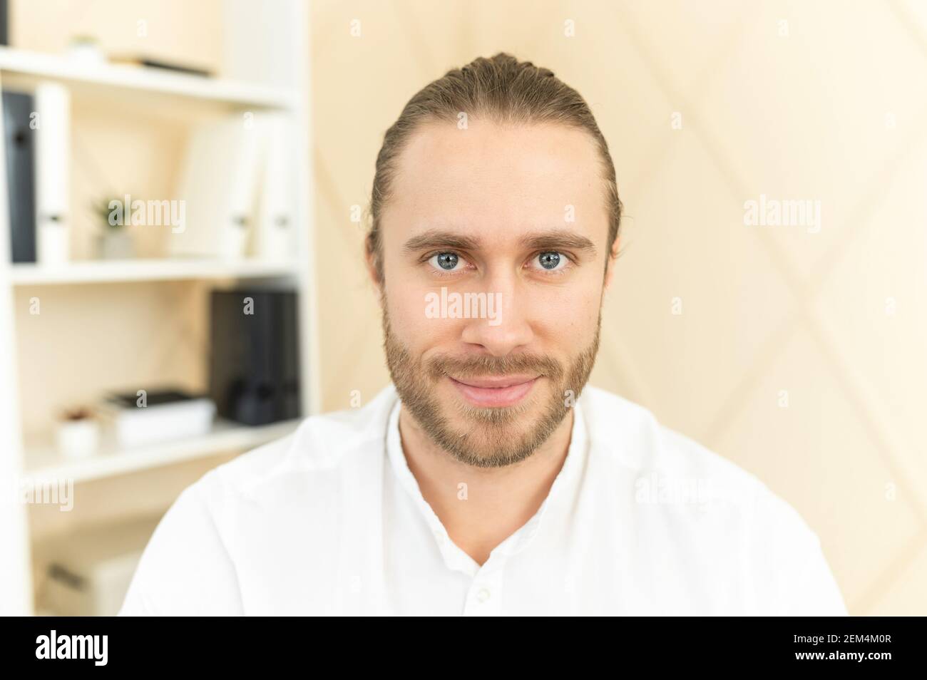 Handsome European man with light brown hair, gray eyes and beard looking at camera, smiling friendly, posing, confident, wearing white formal shirt, workplace, shelf with documents in the background Stock Photo - Handsome European man with light brown hair, gray eyes and beard looking at camera, smiling friendly, posing, confident, wearing white formal shirt, workplace, shelf with documents in the background Stock Photo -