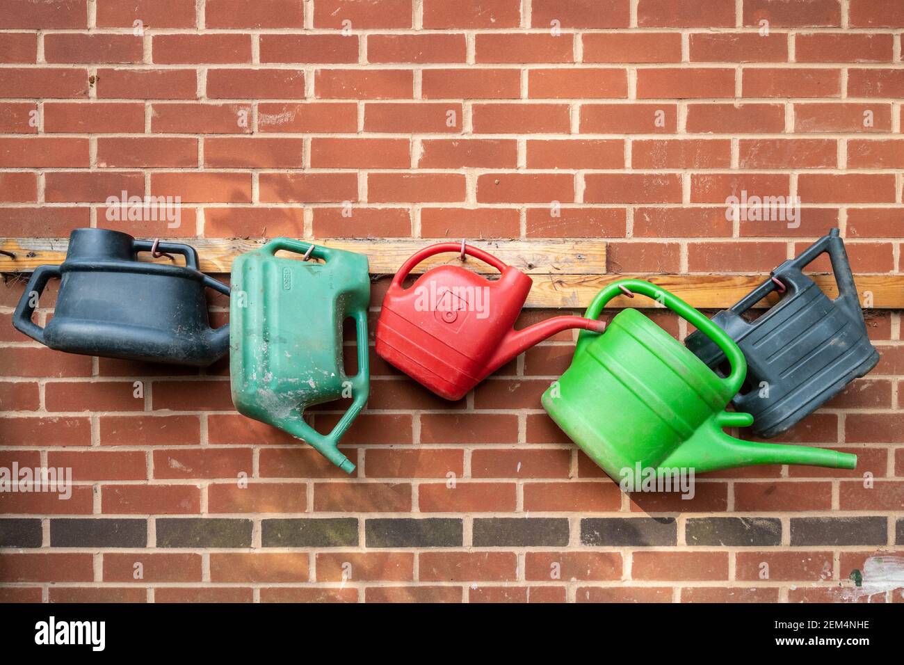 Several colourful watering cans hanging up in a row on a wall Stock Photo