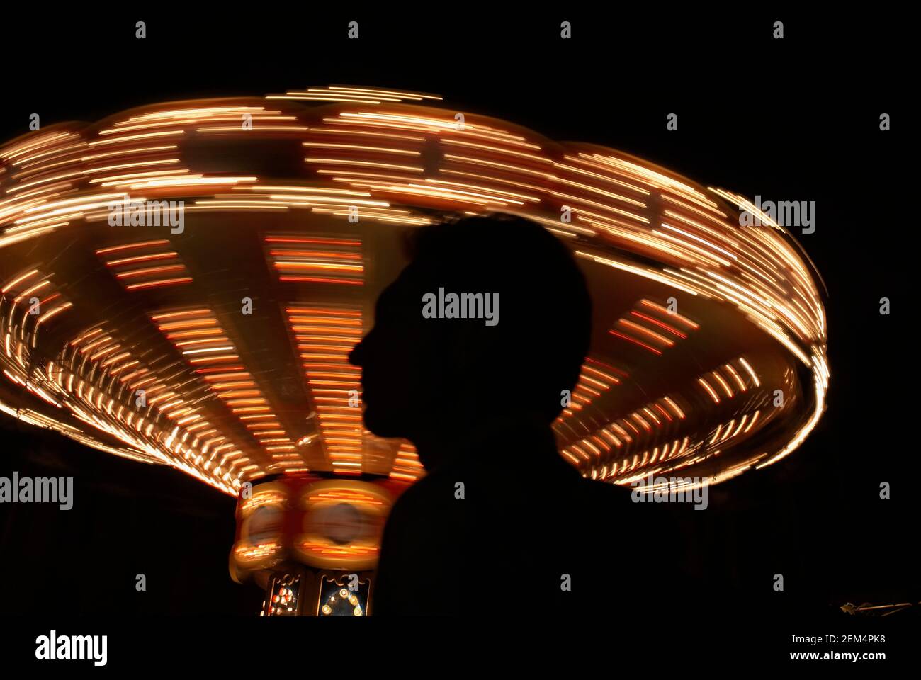 Silhouette of a person in front of a spinning carousel at night Stock Photo