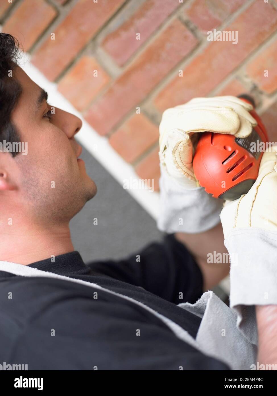Side profile of a young man using a drill on a wall Stock Photo