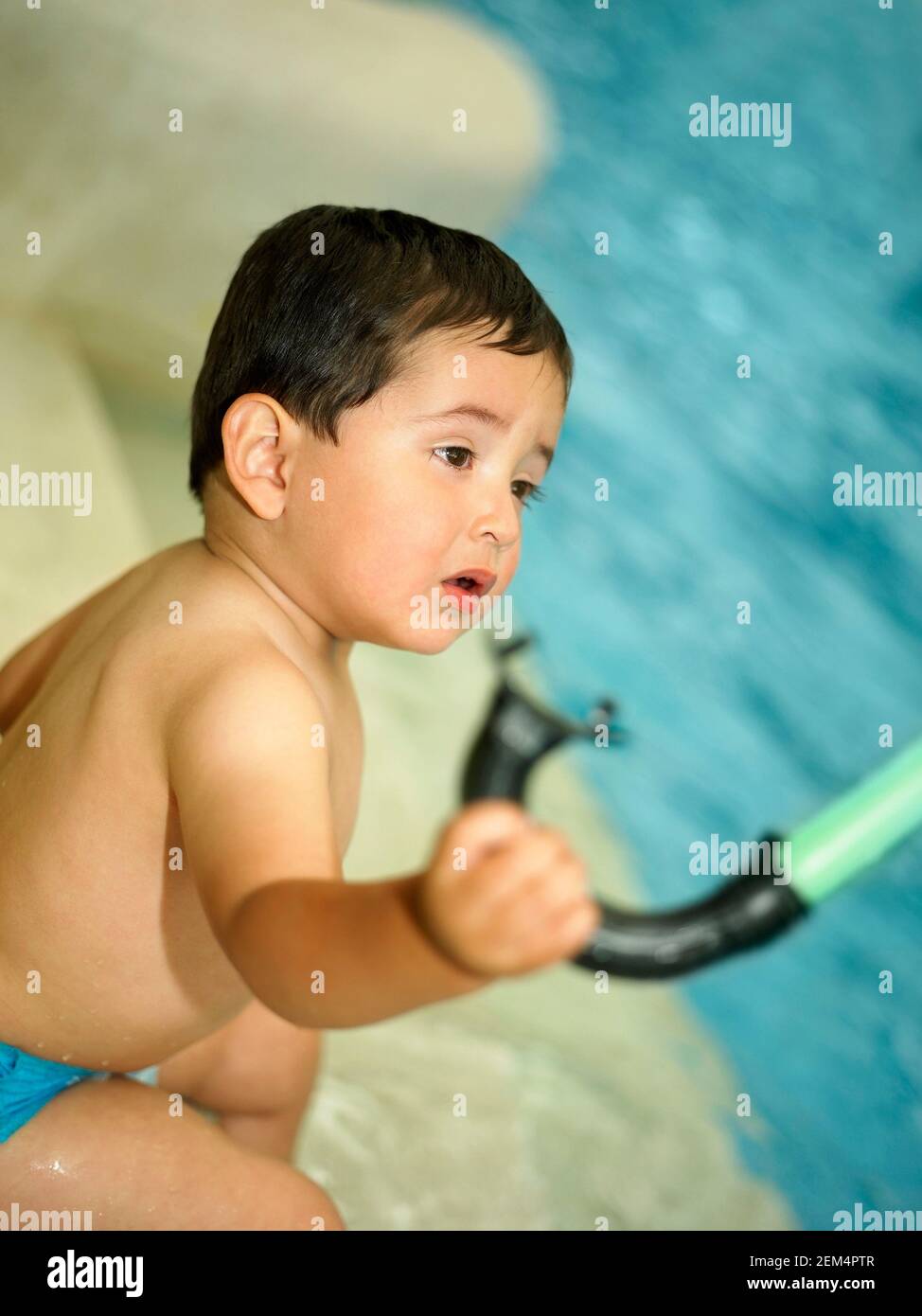 Side profile of a baby boy holding a snorkel and sitting near a swimming pool Stock Photo