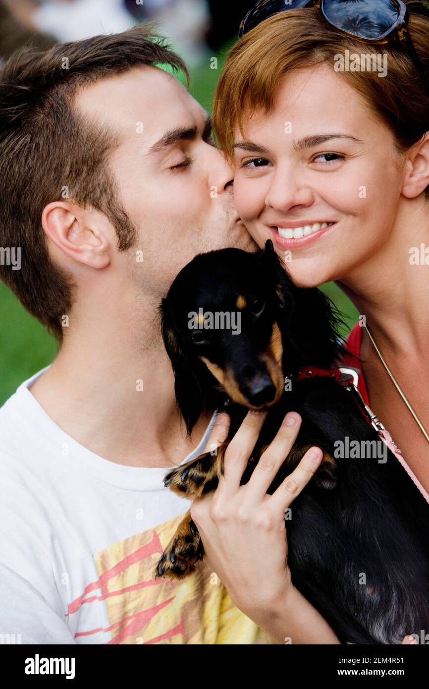 Close-up of a young man kissing a young woman and holding a dog Stock Photo