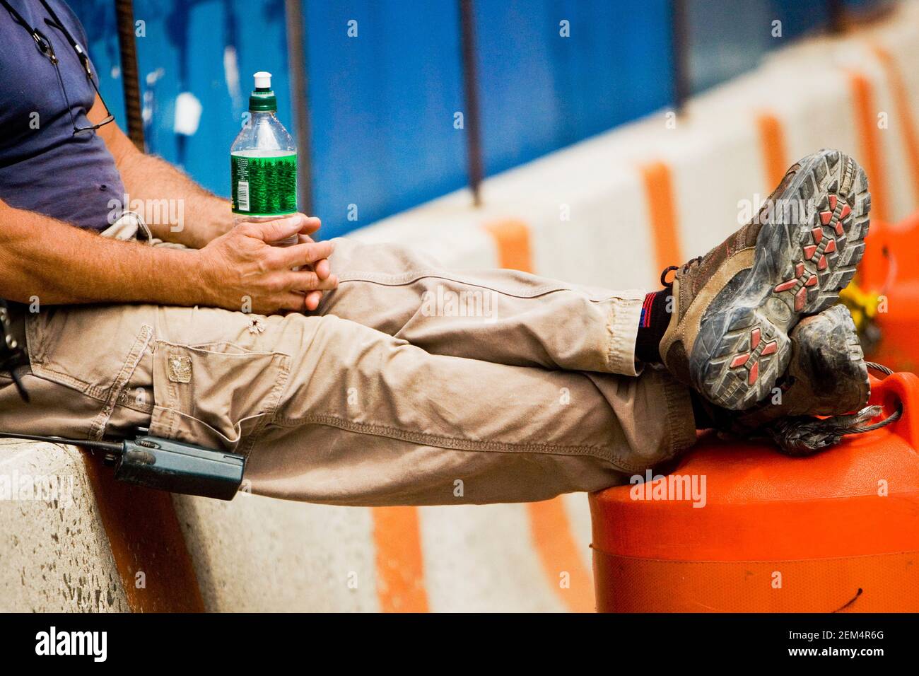 Low section view of a man sitting on a wall and holding a bottle Stock Photo