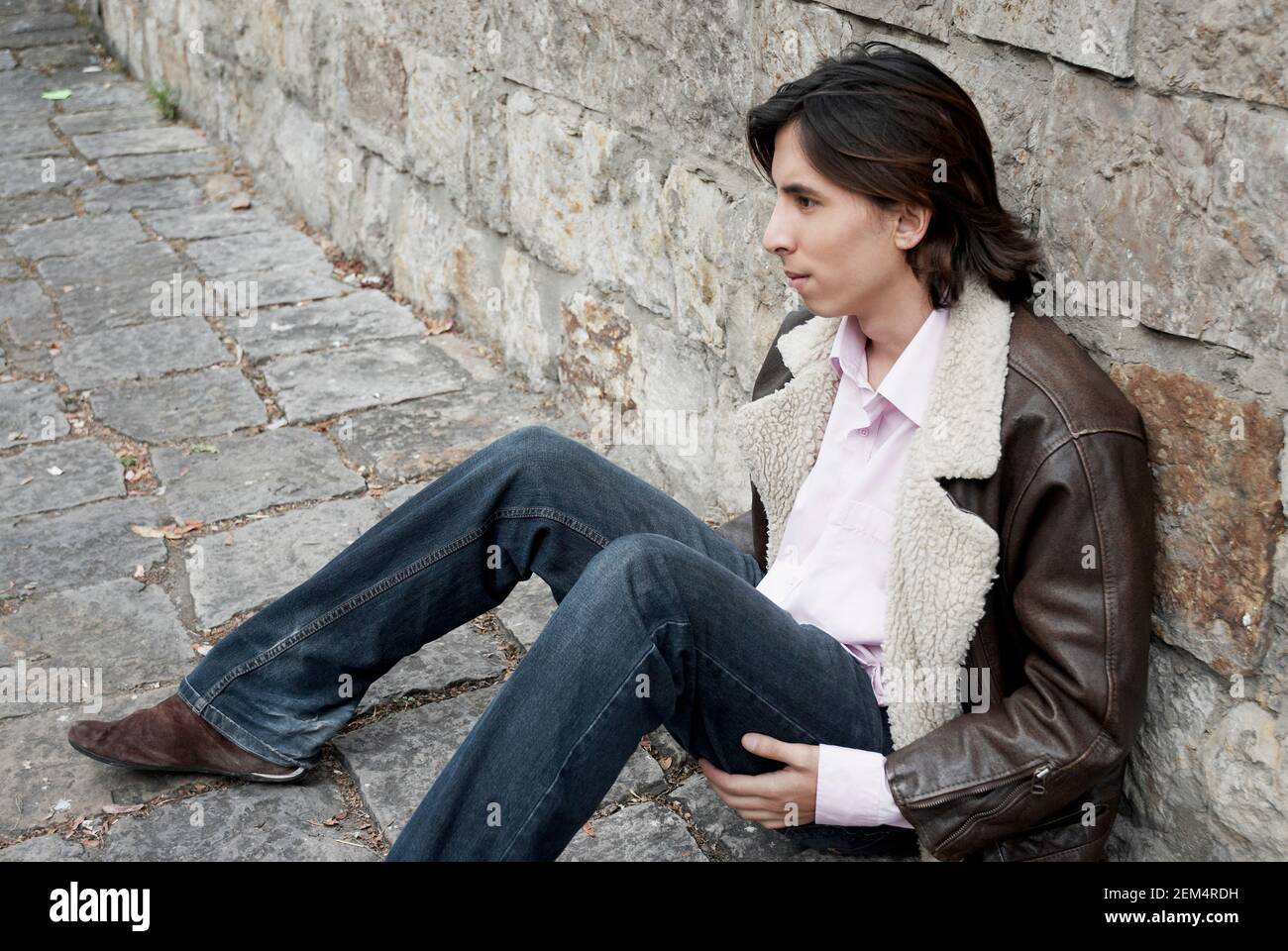 High angle view of a young man leaning against a stone wall and thinking Stock Photo