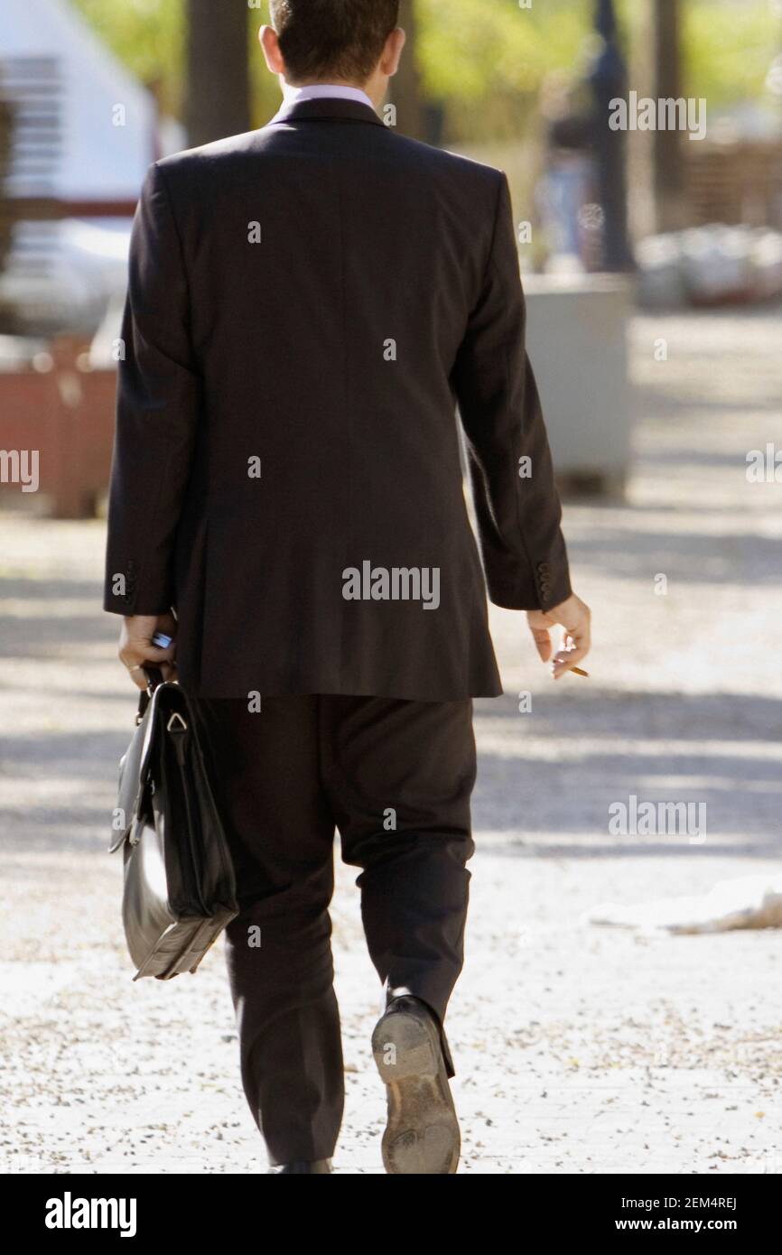 Rear view of a businessman carrying a briefcase and holding a cigarette  Stock Photo