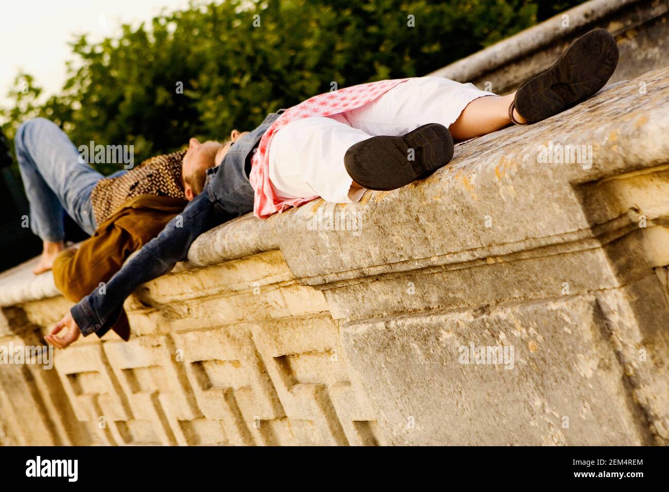 Side profile of a young couple lying on a stone wall Stock Photo