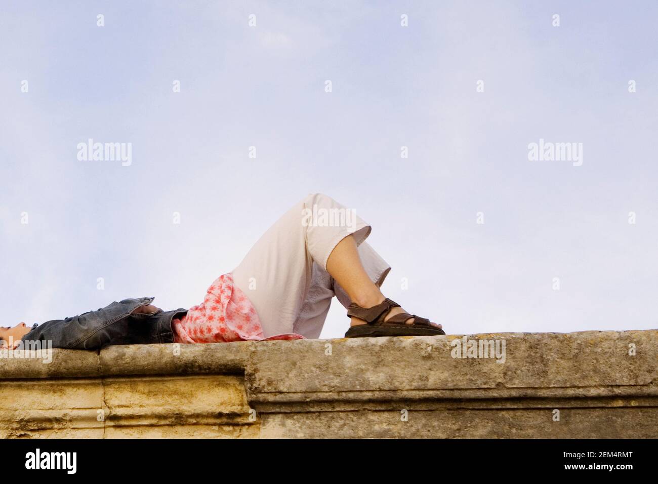 Low angle view of a young woman lying on a stone wall Stock Photo