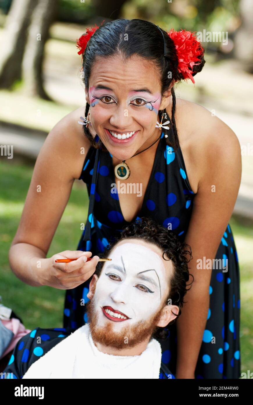 Portrait of a young woman painting a mid adult man's face and smiling Stock Photo