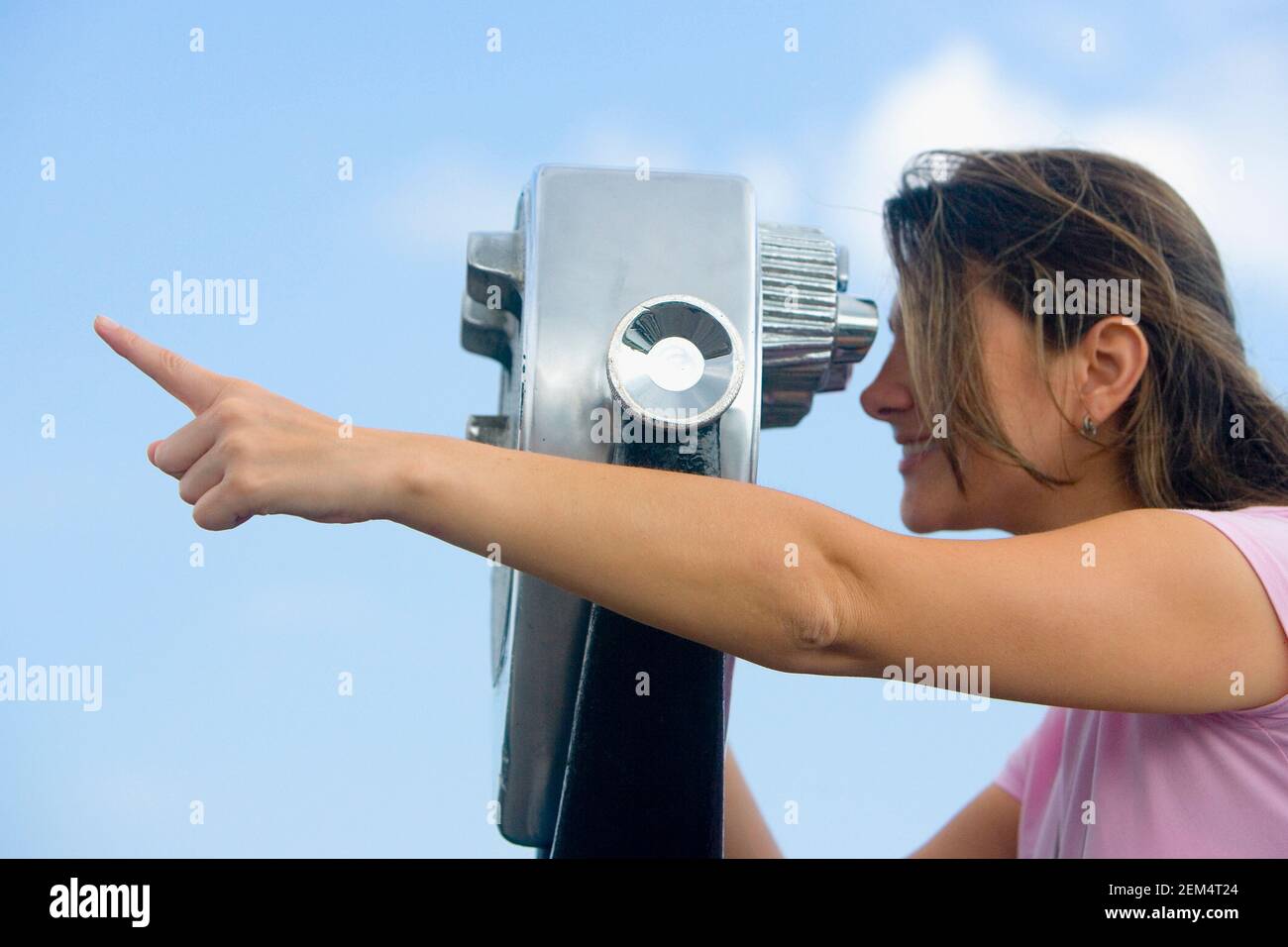 Side profile of a mid adult woman looking through a pair of coin-operated binoculars and pointing forward Stock Photo