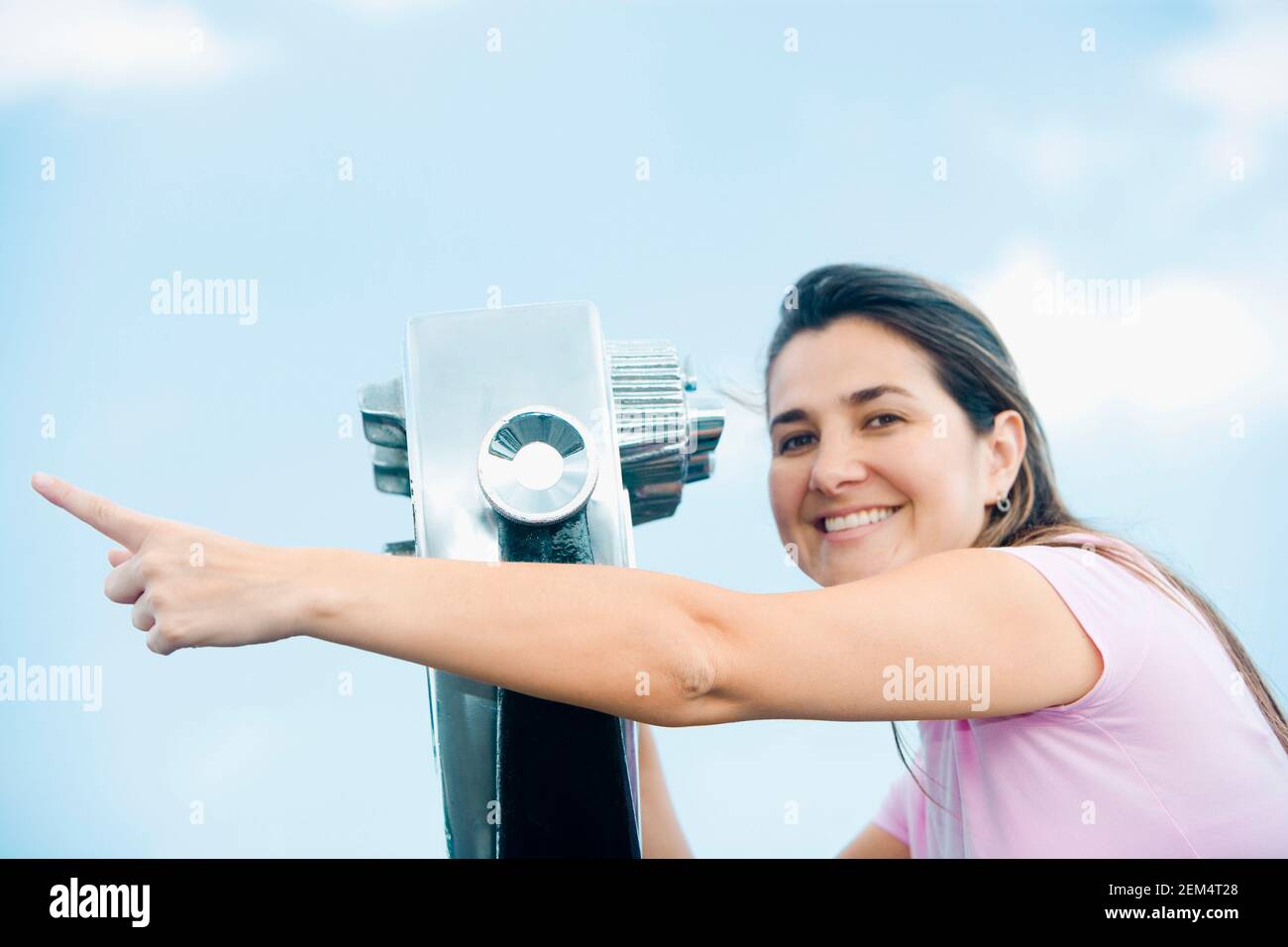 Portrait of a mid adult woman pointing forward near a pair of coin-operated binoculars Stock Photo