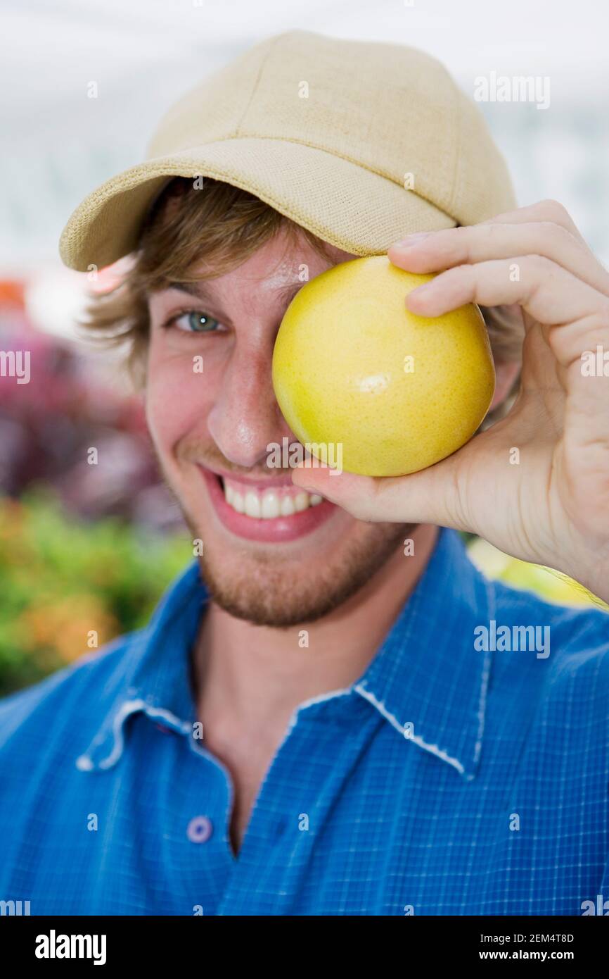 Portrait of a young man holding an orange in front of his eye Stock Photo